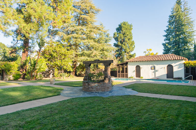 a stone gazebo in a yard with a pool and trees